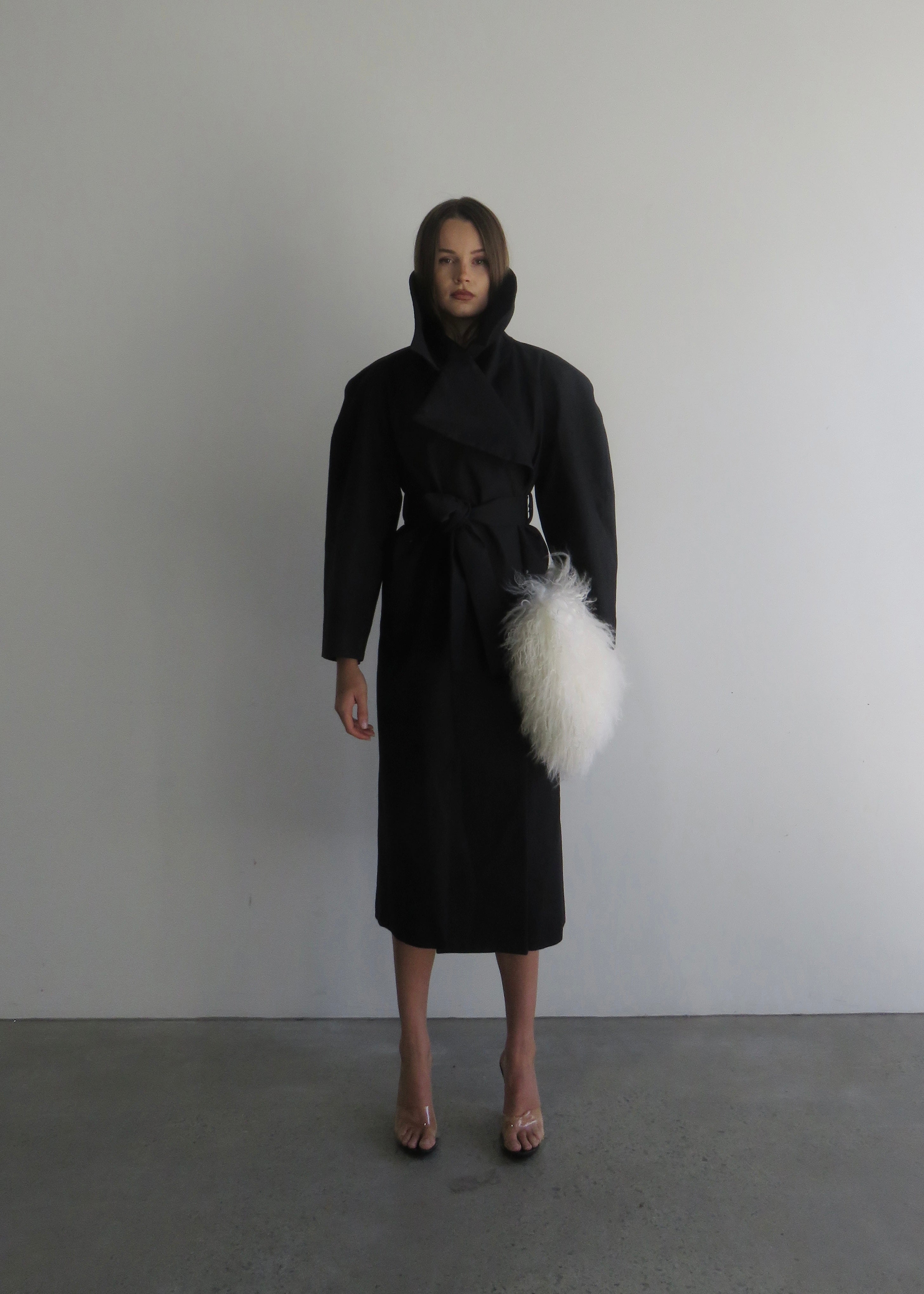 Woman wearing a black coat with a white fur stole against a plain background