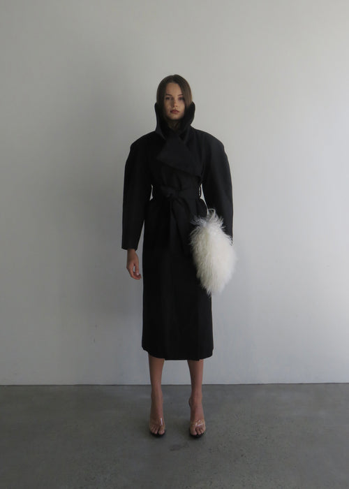 Woman wearing a black coat with a white fur stole against a plain background