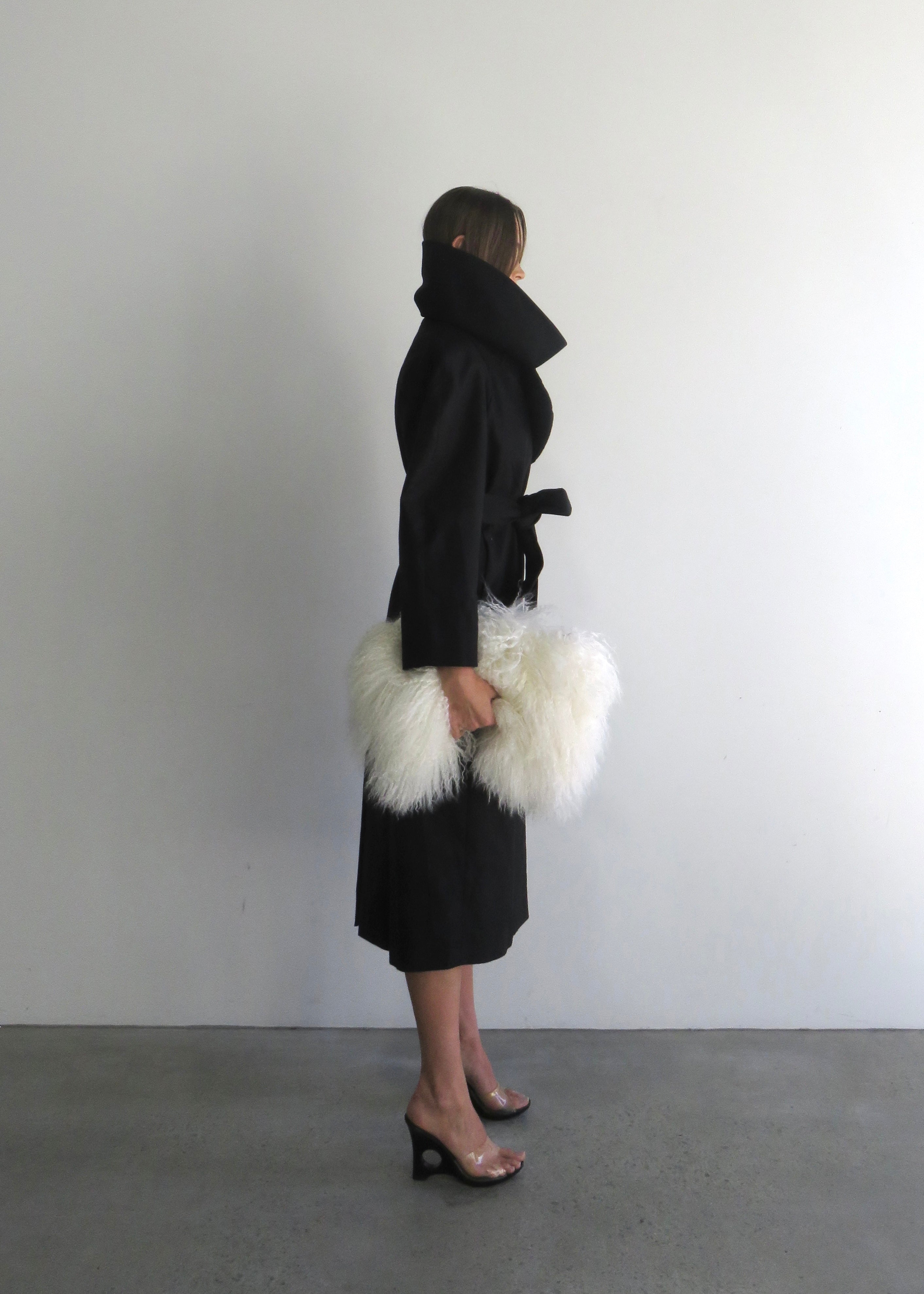 Person wearing a black coat with a white fur-lined hood against a plain background