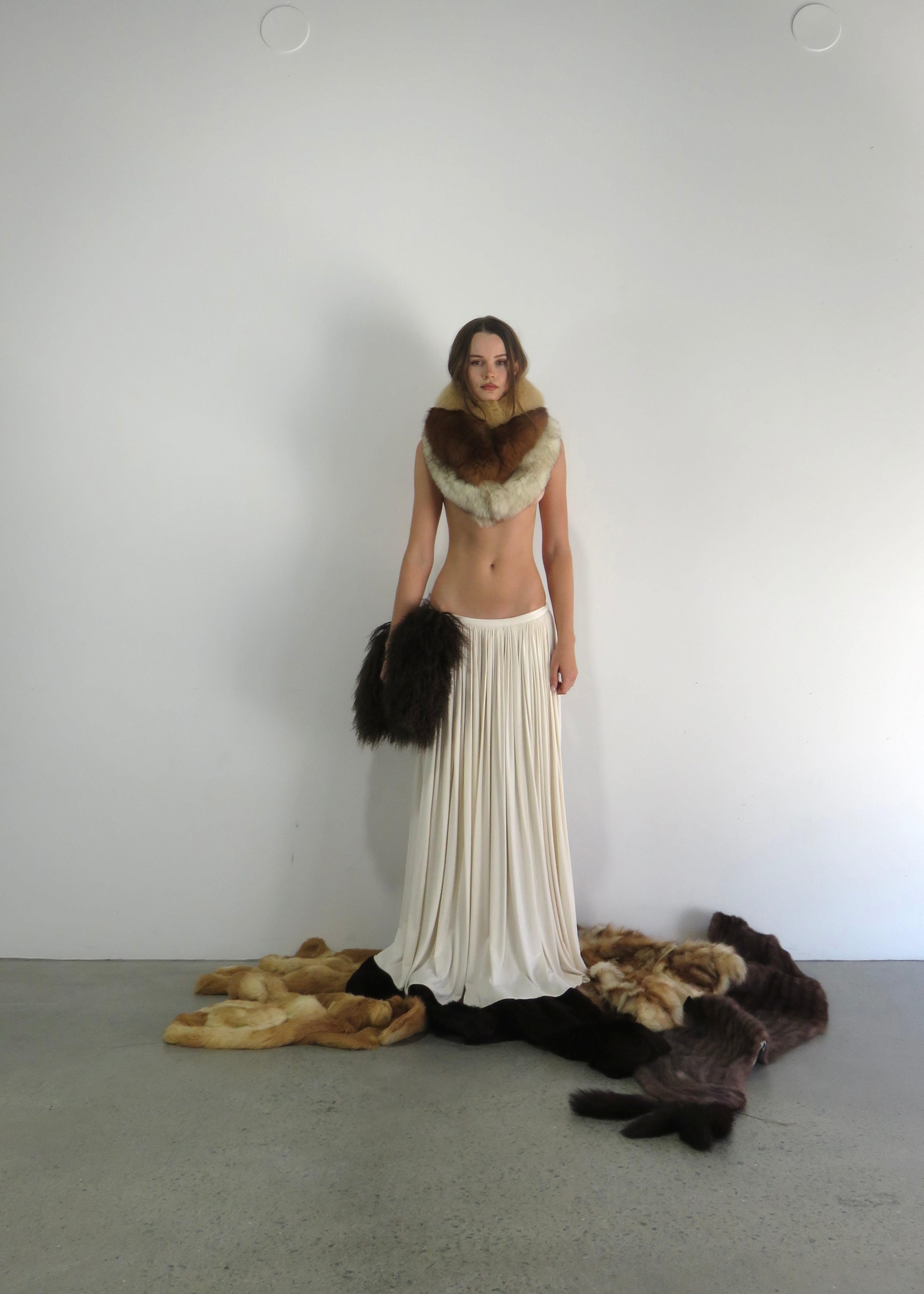 Woman wearing a white dress with fur accents against a plain background