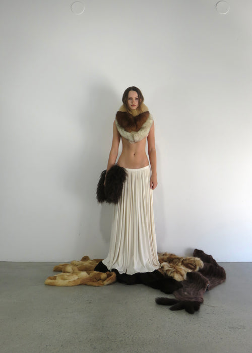 Woman wearing a white dress with fur accents against a plain background