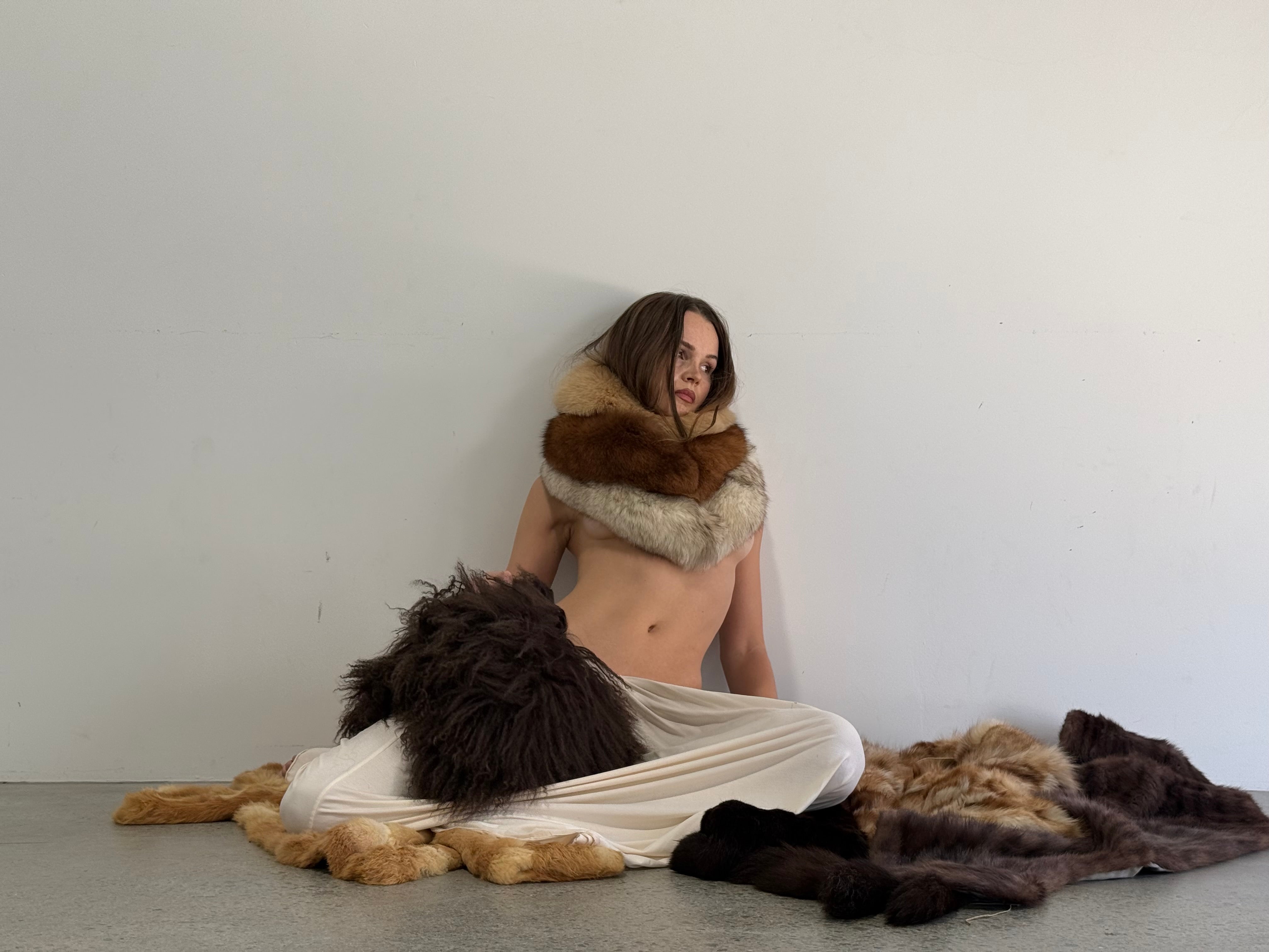 Woman sitting on a bed of fur coats. 
