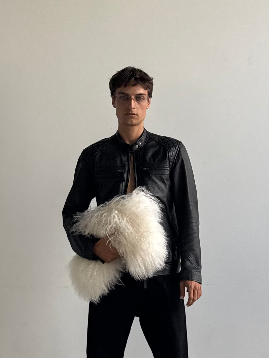 A man wearing black leather jacket, holding a white fur clutch against his chest. 