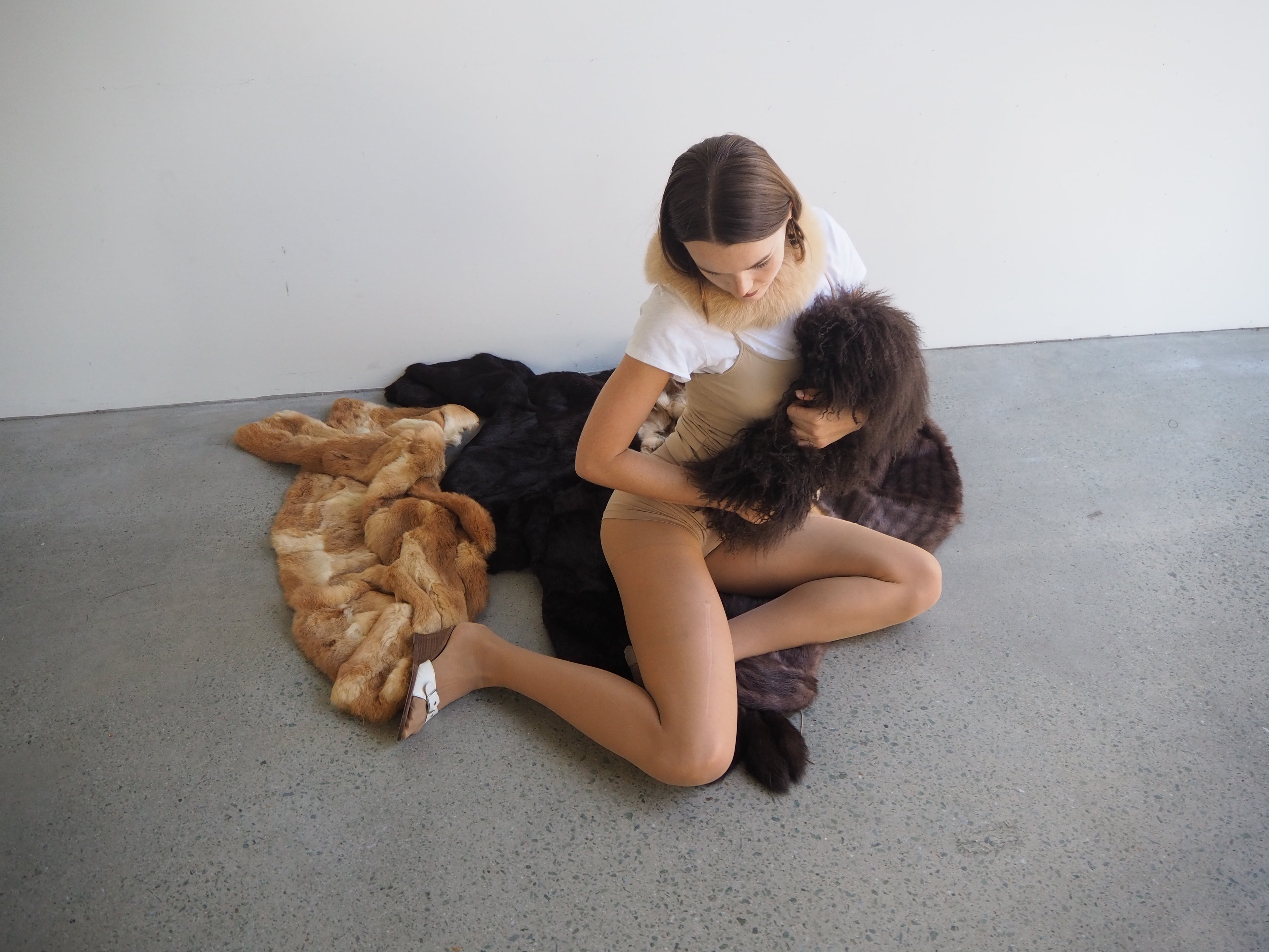 Woman sitting on a concrete floor with fur blankets and a child.
